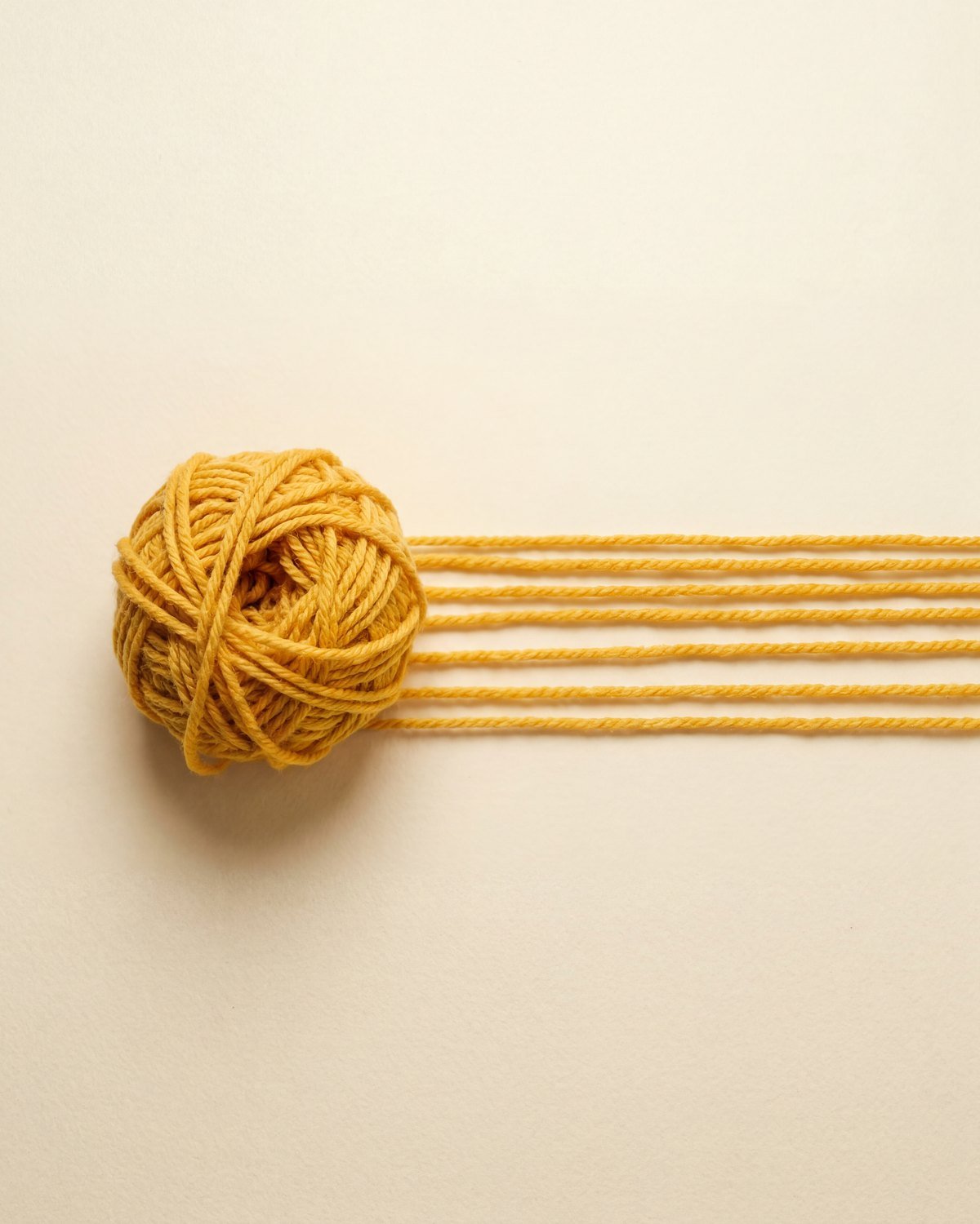 A ball of yellow yarn unraveling into several neat, parallel straight lines across a cream surface